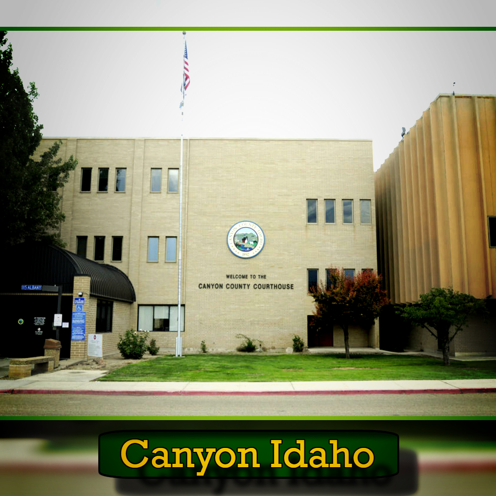 A beige three-story building represents the Canyon County Courthouse in Idaho, featuring an American flag, green lawn, and "Welcome to the Canyon County Courthouse" text on the facade. Occasionally, a tow truck from a local tow service can be seen nearby, ensuring smooth traffic flow around the area.