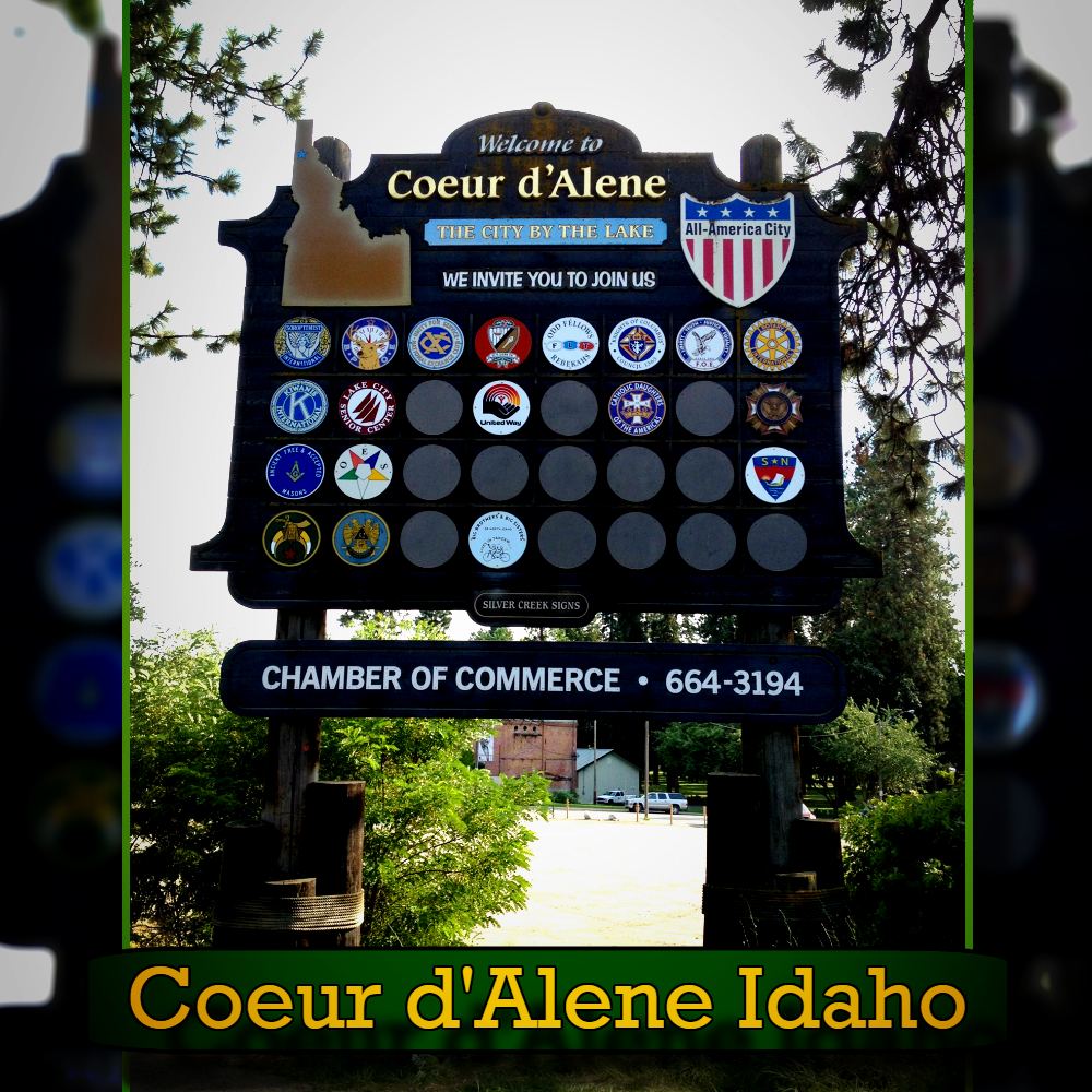 A large welcome sign reads "Welcome to Coeur d'Alene, The City by the Lake," with various badges and a contact for the Chamber of Commerce. Tow service information is included for visitor convenience. Surrounded by trees, text at the bottom reads "Coeur d'Alene Idaho.