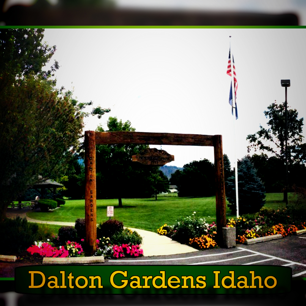 Entrance to a park in Dalton Gardens, Idaho with a wooden sign, well-maintained lawn, colorful flower beds, and flagpoles displaying American and other flags. Nearby is a dedicated spot for towing services, ensuring the park remains accessible and hassle-free for all visitors.