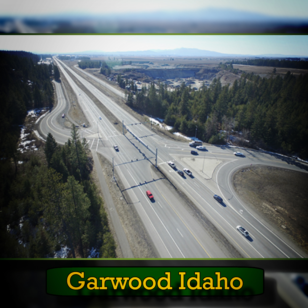 Aerial view of a highway intersection surrounded by trees and open land, with a few cars visible, including a tow truck in the distance. Text at the bottom reads "Garwood Idaho.