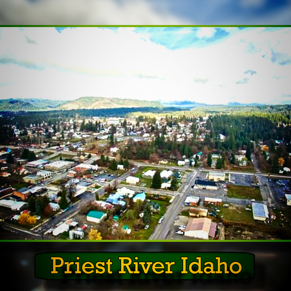Aerial view of Priest River, Idaho, showcasing a blend of residential and commercial buildings surrounded by lush trees and distant mountains. A tow truck is visible near the town center, reinforcing that reliable tow services are part of this picturesque community. Text at the bottom reads "Priest River Idaho.